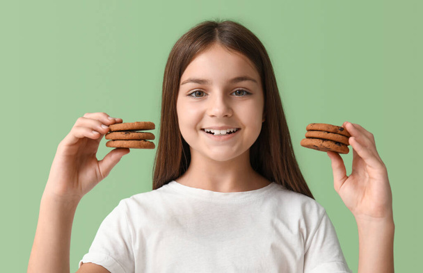 Little girl holding many sweet chocolate cookies on green background - Photo, Image