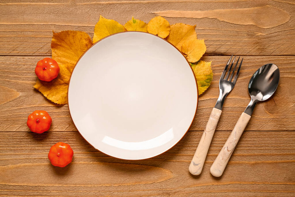 Prázdný talíř s příbory a podzimními listy na dřevěném pozadí - Fotografie, Obrázek