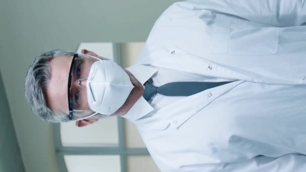 Retrato de un científico masculino con respirador y gafas con bata de laboratorio blanca mientras mira la cámara. Cruzando las manos y de pie en la sala de laboratorio. Trabajando en el centro de desarrollo. Concepto hospitalario. - Metraje, vídeo