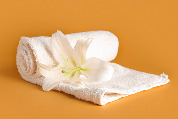 Ролл чистое полотенце и красивый цветок лилии на цветном фоне - Фото, изображение