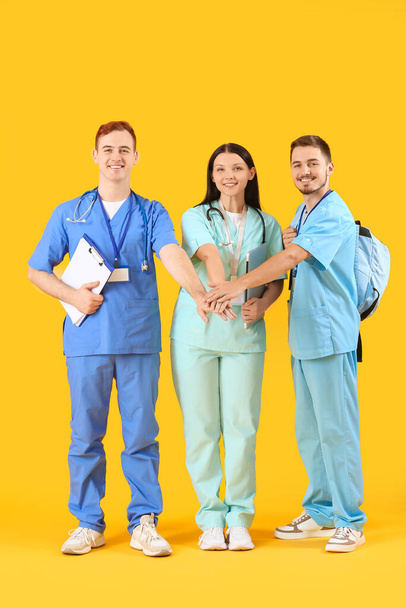 Φοιτητές ιατρικής να βάλει τα χέρια μαζί σε κίτρινο φόντο - Φωτογραφία, εικόνα