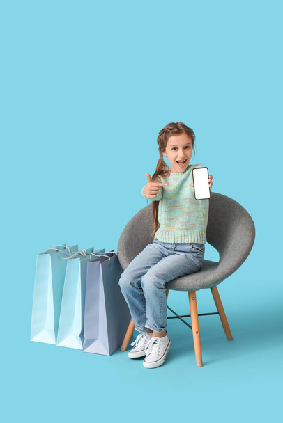 Pieni tyttö ostoskassit istuu tuolilla sinistä taustaa vasten - Valokuva, kuva
