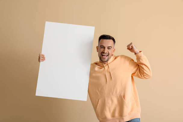 Ευτυχισμένος νεαρός άνδρας με λευκή αφίσα σε μπεζ φόντο - Φωτογραφία, εικόνα