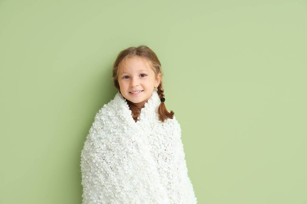 schattig klein meisje in warme deken op groene achtergrond - Foto, afbeelding