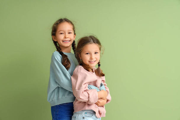 Leuke kleine meisjes in sweatshirts knuffelen op groene achtergrond - Foto, afbeelding