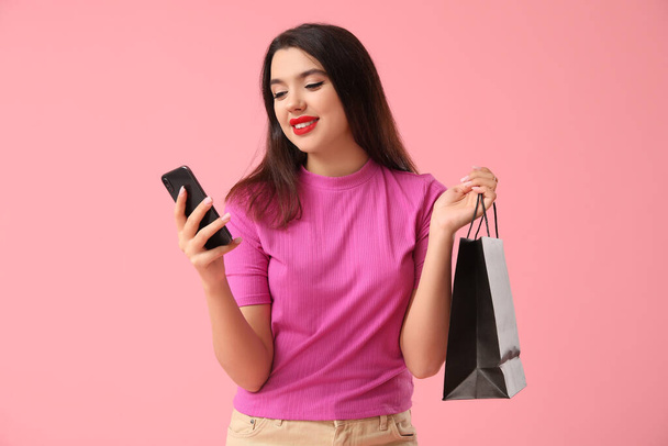 Beautiful young woman with shopping bag and mobile phone on pink background. Black Friday sale - Photo, Image