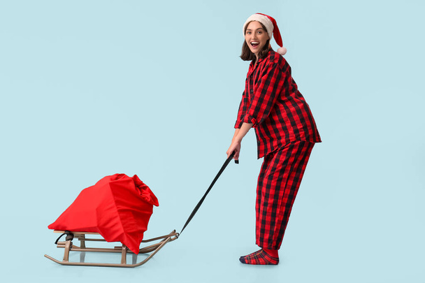 Pijamalı, Noel Baba çantalı, mavi arka planda genç ve güzel bir kadın. - Fotoğraf, Görsel