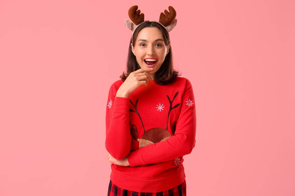 Beautiful young woman in pajamas and Christmas deer horns on pink background - Photo, Image