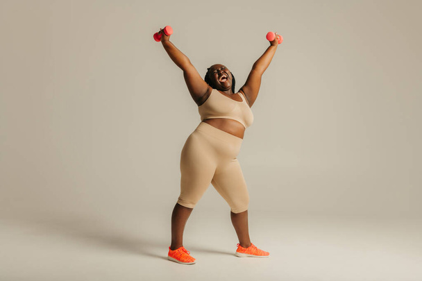Confident plus size African woman in sportswear radiating confidence while exercising on studio background - Photo, Image