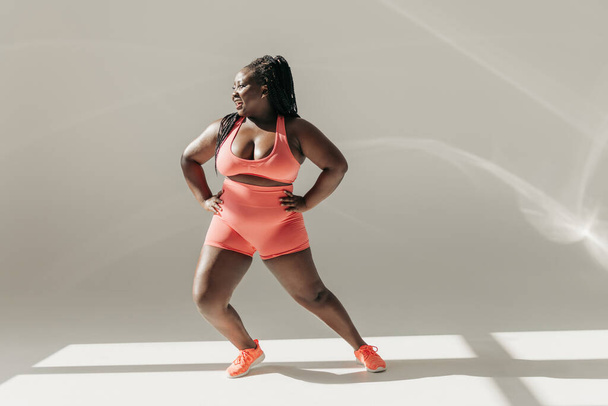 Full length of happy African plus size woman in sportswear warming up before training in fitness studio - Photo, Image