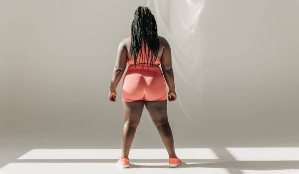 Full length rear view of African plus size woman in sportswear standing in fitness studio - Foto, imagen