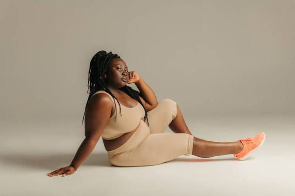 Beautiful plus size African woman in sportswear looking confident while sitting against studio background - Fotografie, Obrázek