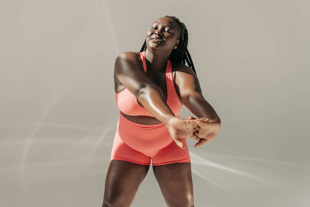 Beautiful African plus size woman in sportswear doing stretching exercises in fitness studio - Photo, Image