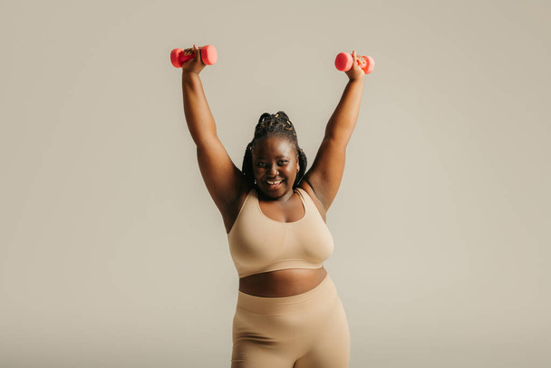 Beautiful curvy African woman in sportswear radiating confidence while exercising on studio background - Фото, изображение