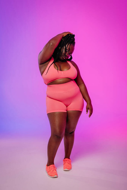 Full length of confident African plus size woman in sportswear standing against colorful background - Foto, Imagem