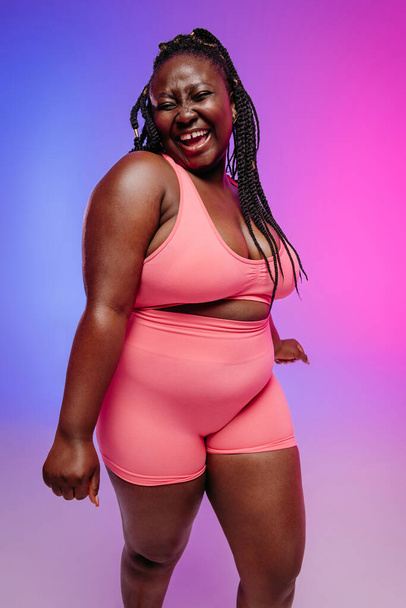 Happy plus size woman in sportswear radiating love to her body while dancing on vibrant background - Foto, Bild