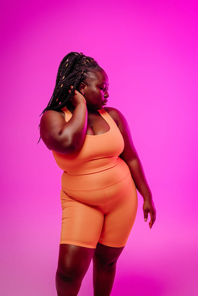 Confident African plus size woman in sportswear holding hand in hair against color background - Fotografie, Obrázek
