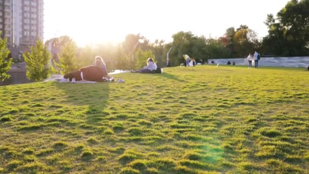 Lidé relaxovat ve veřejném parku s jezerem a zelené stromy s mrakodrapy Budovy ve městě na pozadí a jasné slunce západu slunce. Park pro odpočinek, volný čas a zábavu v centru moderní metropole. - Záběry, video