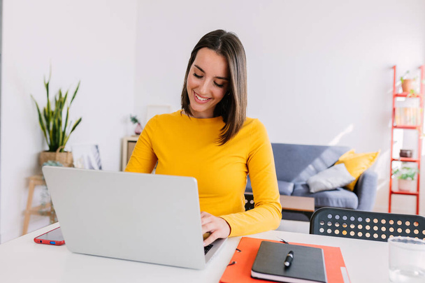 Szczęśliwa młoda, ładna kobieta pracująca na laptopie w domu. Tysiącletnie dorosłe kobiety uczą się online. Edukacja i koncepcja biznesu. - Zdjęcie, obraz