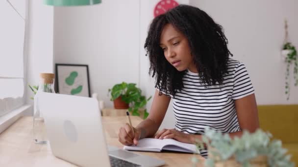 Jonge Braziliaanse studente die aantekeningen maakt terwijl ze thuis een laptop gebruikt. Millennial latin krullende vrouw leren online luisteren virtuele video oproep. Bedrijfs- en onderwijsconcept. - Video