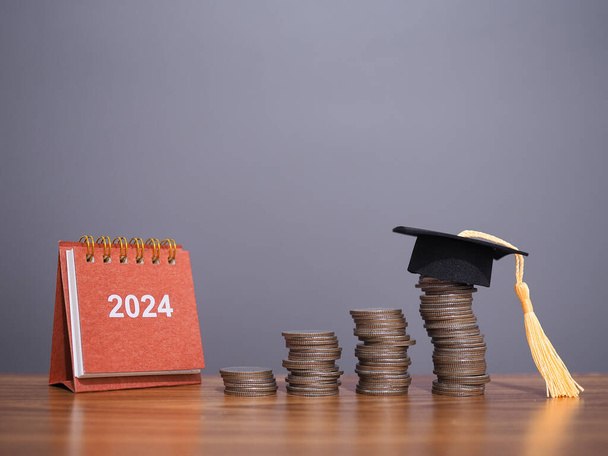 Study goals, 2024 Desk calendar with graduation hat on stack of coins. The concept of saving money for education, student loan, scholarship, tuition fees in New Year 2024 - Photo, Image