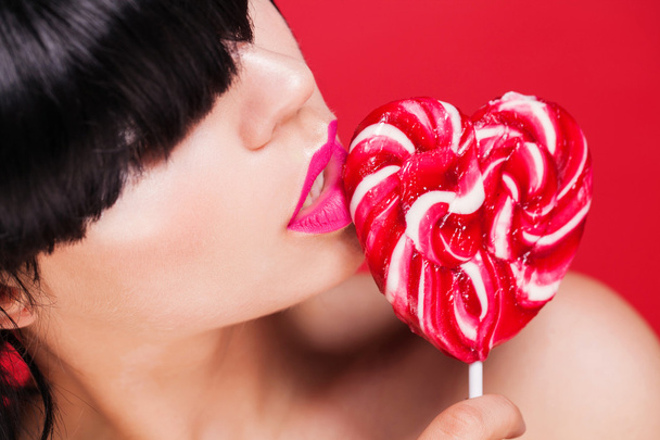 Closeup photo of a beautiful sexy red lips with lollipop - 写真・画像