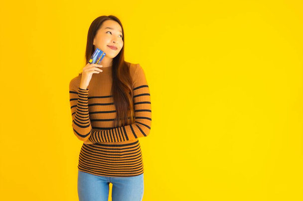Портрет красивая молодая азиатская женщина использовать смартфон или сотовый телефон с кредитной картой для покупок в Интернете на желтом изолированном фоне
 - Фото, изображение