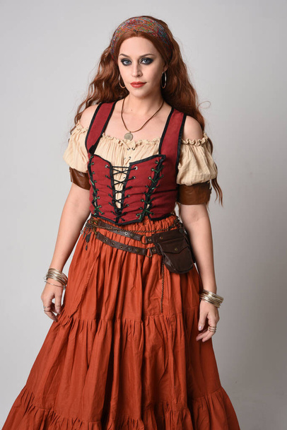 close-up portret van een mooie roodharige vrouw in een middeleeuws meisjeskostuum, waarzegster. Poseren met gebaren handen reiken, dansen, geïsoleerd op studio achtergrond. - Foto, afbeelding