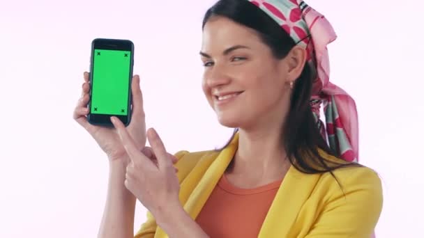 Happy woman, phone and pointing to green screen in advertising or marketing against a studio background. Portrait of female person smile, OK emoji or showing mobile smartphone app, display or mockup. - Footage, Video