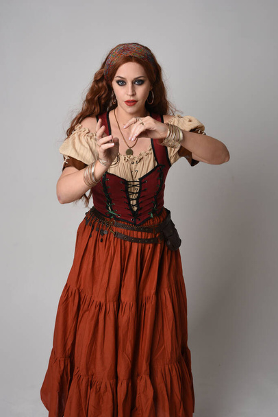 zbliżyć portret pięknej rudej kobiety w średniowiecznym stroju wróżki. Pozowanie z gestykulacyjnymi dłońmi sięgającymi, tańczącymi, odizolowanymi na tle studia. - Zdjęcie, obraz