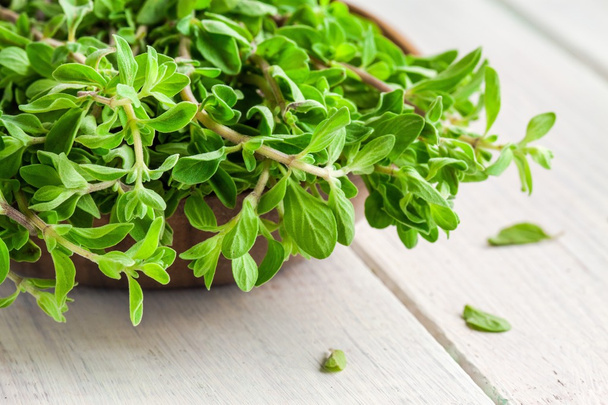 Majoránka syrové zelené byliny v misce na bílý dřevěný stůl - Fotografie, Obrázek