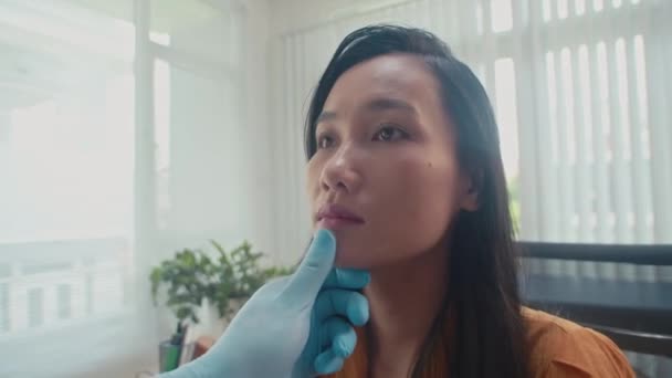 Blisko azjatyckich kobiet twarz jest badana przez chirurga plastycznego w rękawiczkach medycznych w klinice - Materiał filmowy, wideo