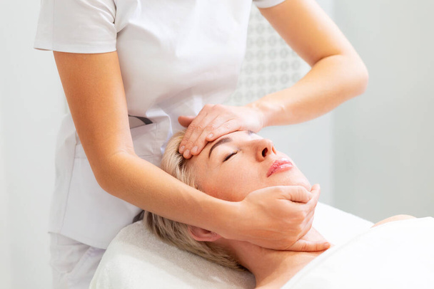 Um cosmetologista massageia o rosto de uma bela mulher adulta. Rejuvenescimento e cosmetologia profissional no salão. - Foto, Imagem