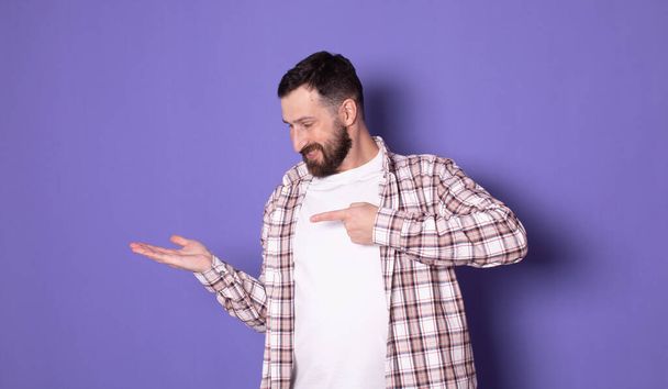 Handsome bearded trendy stylish confident positive cheerful man pointing on blank copy space, over pastel violet purple background            - Foto, afbeelding