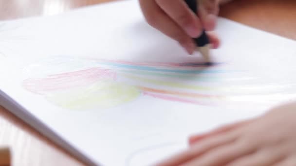 Un bambino in età prescolare disegna con matite colorate in un album. Mano del bambino con un primo piano a matita, messa a fuoco selettiva. La ragazza disegna un arcobaleno - Filmati, video