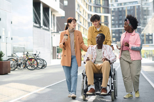 Молоді люди, які ходять по місту зі своїм другом з інвалідністю - Фото, зображення