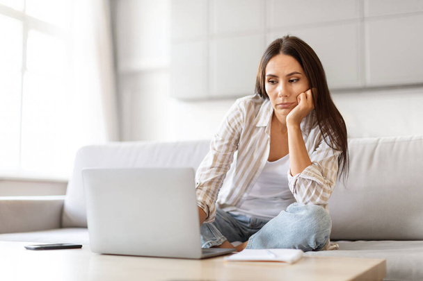Ideges fiatal nő néz laptop számítógép, miközben ül a kanapén otthon, unatkozó Y-generációs nő dolgozik, vagy tanulmány Online, miután hiányzik az inspiráció, szenvedés kreativitás válság, másolás tér - Fotó, kép