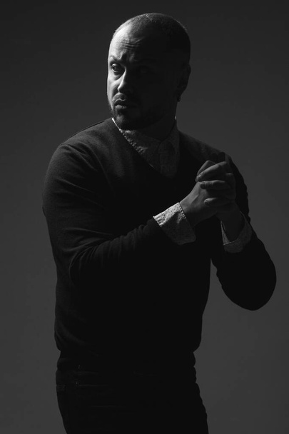 Drama concept. Portrait of disturbed charismatic 40-year-old man standing over black background. Short haircut. Classic, smart casual style. Black and white studio shot - Foto, Imagem