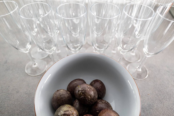 Copos de champanhe ou taças de champanhe alinhadas em uma bancada de cozinha em uma festa com maracujá fresco em uma tigela. - Foto, Imagem
