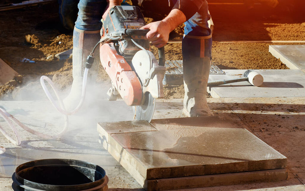 Le constructeur coupe des dalles de béton avec une scie à essence et une lame de diamant pendant les travaux de pavage de sentiers extérieurs close up - Photo, image