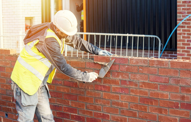 Tvrdě pracující zedník klade cihly na betonovou směs na staveništi. Boj proti bytové krizi výstavbou cenově dostupnějších domů - Fotografie, Obrázek