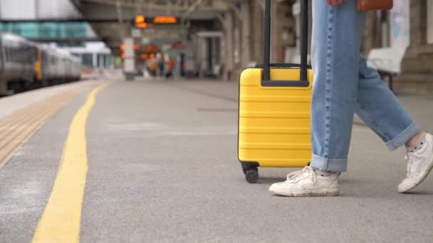 Viajero con una maleta amarilla esperando un tren en la estación de tren en el andén. Concepto de viaje. - Metraje, vídeo