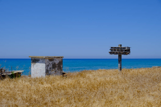 Εγκαταλελειμμένη ξύλινη φωλιά περιστεριών και άλλες κατασκευές σε χωράφι με κριθάρι με θέα τη θάλασσα στο χωριό Αργάκα στην Κύπρο - Φωτογραφία, εικόνα