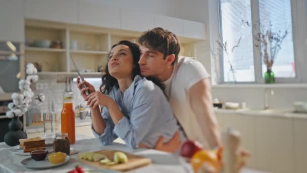 Szczęśliwa para rozmawia na przytulnej kuchni gotowanie rodzinne śniadanie z bliska. Romantyczny kochający mąż przytulający piękną żonę przygotowującą smaczne jedzenie rano. Pojęcie szczęśliwości związku małżeńskiego. - Materiał filmowy, wideo