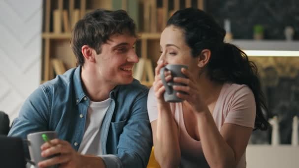 Nyugodt házastársak beszélgetnek a kényelmes nappaliban, közelről. Boldog mosolygós pár, akik otthon tartják a kávéscsészét. Szerető pár élvezi a nyugodt családi estét együtt. A kapcsolat fogalma - Felvétel, videó