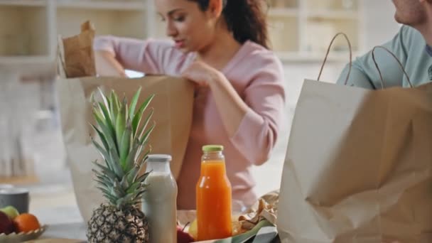 Paar uitpakken afgeleverde producten staan bij gezellige keuken samen close up. Glimlachende echtgenoten die biologische maaltijden uit papieren pakjes halen op het aanrecht. Online supermarkt winkelen diensten concept. - Video