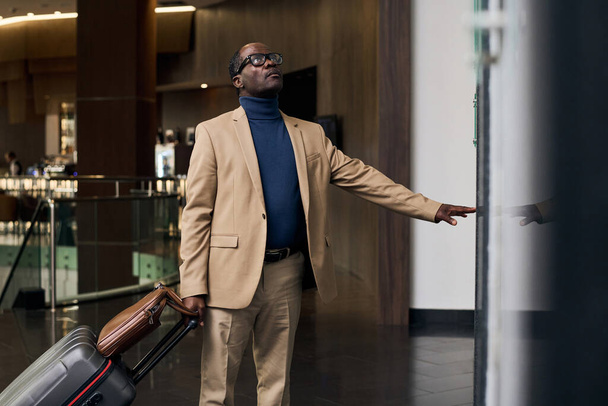 Afrikkalainen amerikkalainen mies matkatavarat painamalla nappia ja odottaa hissiä - Valokuva, kuva