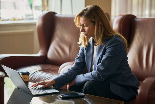 Üzletasszony online dolgozik a laptopon, miközben ül a kanapén a szálloda halljában - Fotó, kép