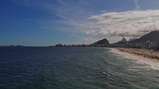 Drohnenaufnahmen vom Copacabana-Strand in Rio de Janeiro Brasilien. Das Video beginnt über dem Meer mit Blick auf das Ende der Bucht und wendet sich langsam dem Strand und der Stadt dahinter zu. - Filmmaterial, Video