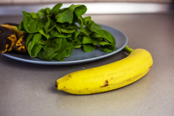 banaani on tiskillä vieressä lautasellinen pinaattia ja kaksi ylikypsää banaania - Valokuva, kuva